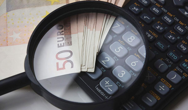 Magnifying glass over a calculator with a stack of 50 euro notes, implying financial analysis or budgeting.