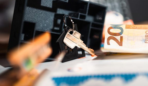 Key inserted into a keyhole with a 20-euro banknote beside it on a desk, suggesting security or money-related risk.