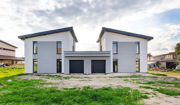 Symmetrical modern two-story duplex with a central double garage, gray and white facade, large windows, on a grassy lot.