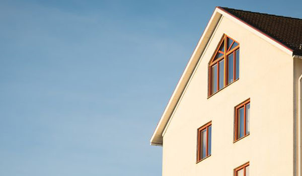 Cream-colored house with a triangular gable window against a clear blue sky, showcasing brown window frames.